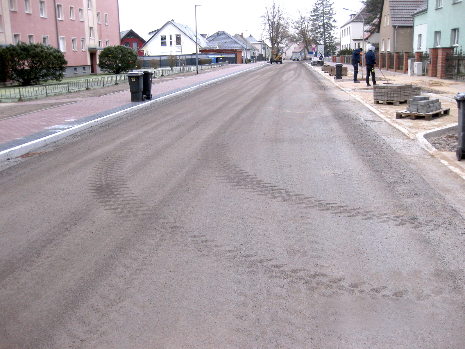 Fertiggestellte Fahrbahn der B 122 in Alt Ruppin, Bauarbeiter fegen Sand in die Fugen zwischen den Pflastersteinen der Einfahrten zu den Grundstücken und auf den Gehwegen